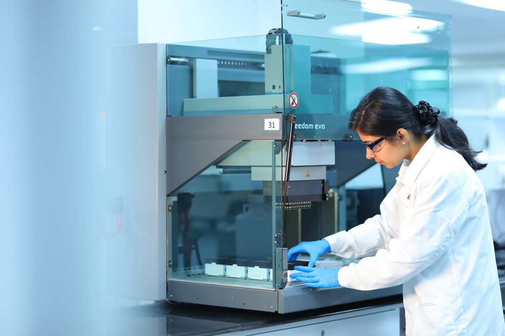 Scientist in a lab coat and safety glasses working with a Tecan Freedom EVO liquid handling system, conducting in vitro ADME assays for drug metabolism and pharmacokinetics (DMPK) research.