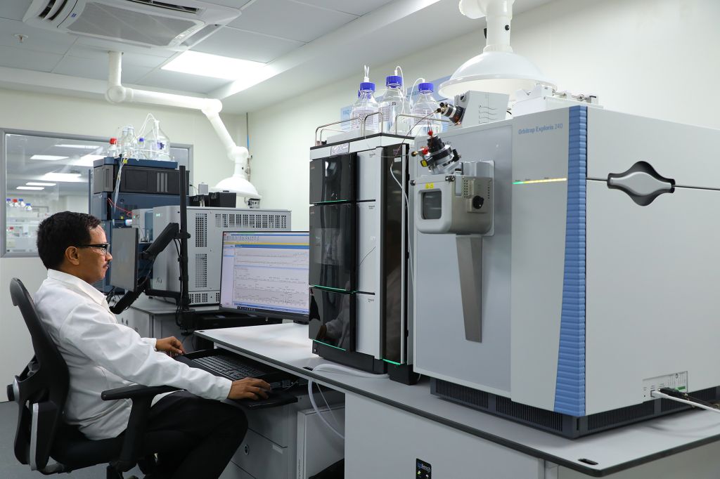 Scientist working on a computer in a laboratory equipped with advanced analytical instruments, including a high-performance mass spectrometer, used for bioanalytical services in DMPK research.