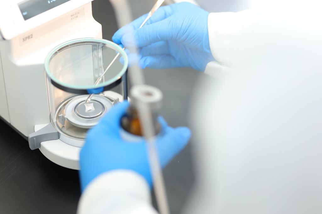 Scientist wearing blue gloves handling a sample with precision using a microbalance in a laboratory setting, representing compound management in DMPK research.