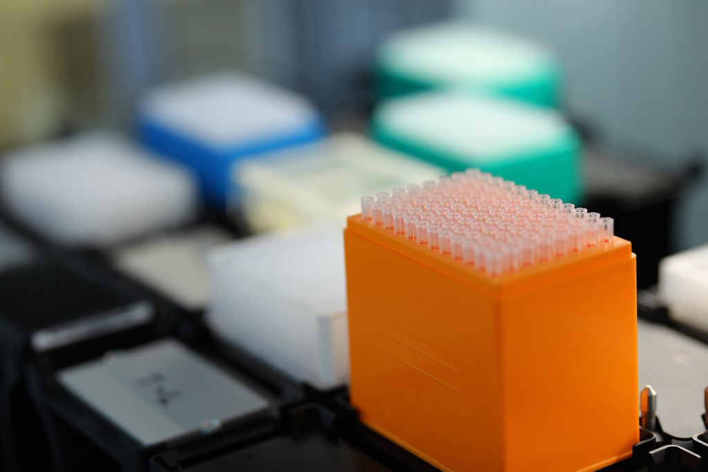 Close-up of a laboratory pipette tip rack with multiple transparent tips, set against a blurred background of colorful lab equipment in a pharmaceutical research setting.